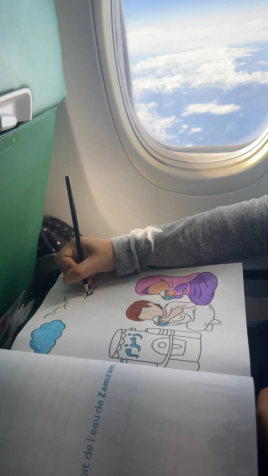 Enfant coloriant dans le cahier de coloriage Omra pendant le voyage en avion