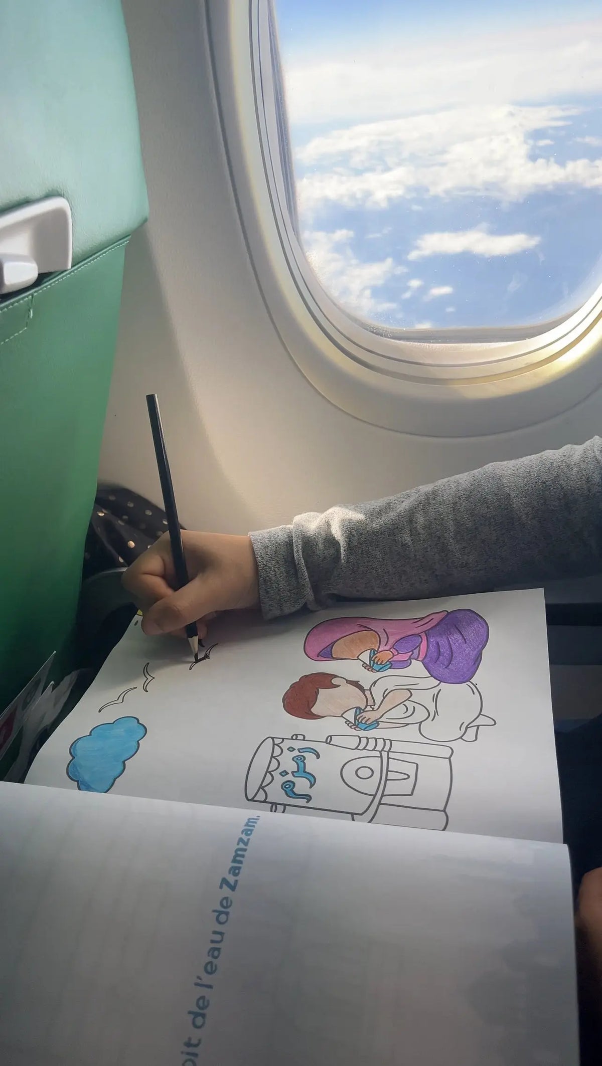 Enfant coloriant dans le cahier de coloriage Omra pendant le voyage en avion